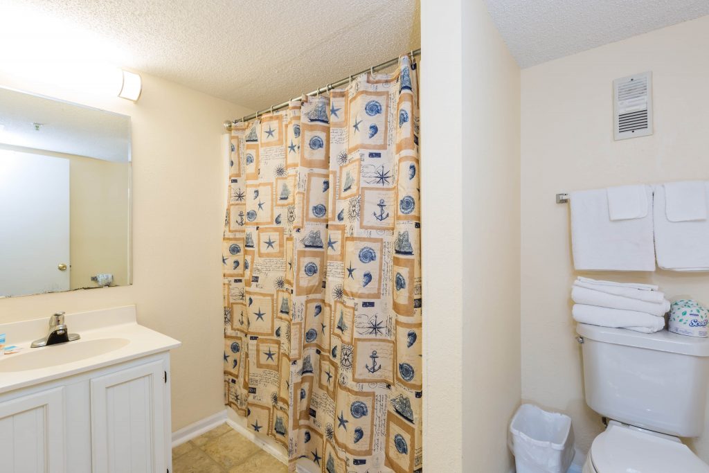 A bathroom with a nautical-themed shower curtain, a toilet with towels, and a sink with a mirror.