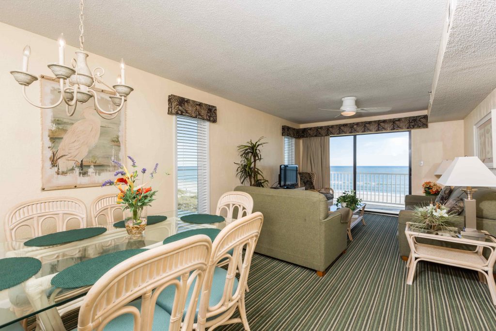 A wide view of a suite's living and dining area with a balcony and ocean view.