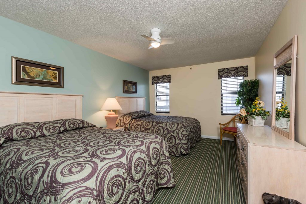 A hotel room with two beds, a dresser with a mirror, and a ceiling fan.